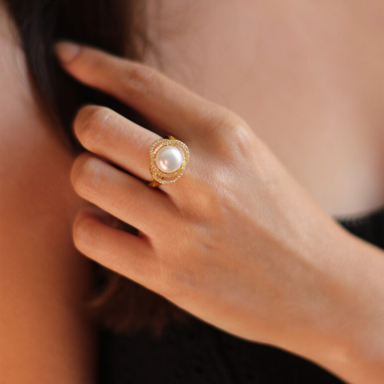 Woman wearing Marette altair pearl ring, white topaz stones hand set around a Freshwater pearl with yellow gold plated Sterling Silver.